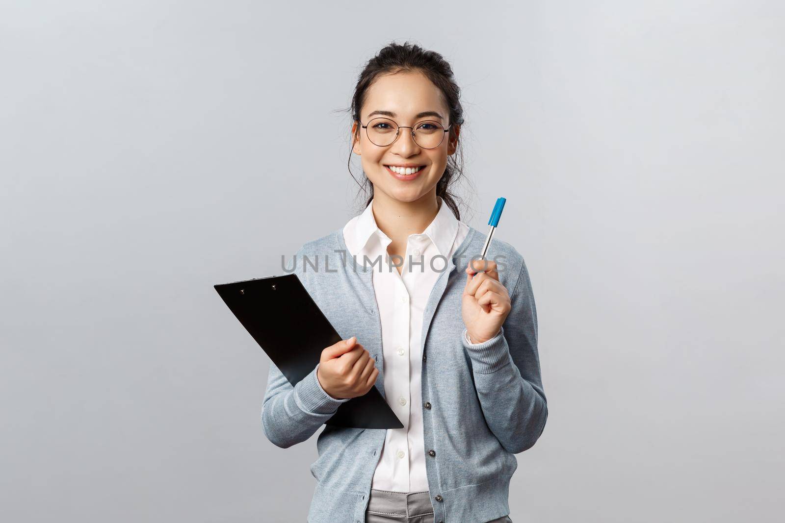 Education, teachers, university and schools concept. Cheerful asian woman in glasses, office lady employee holding pen and clipboard, secretary writing down info during business meeting by Benzoix