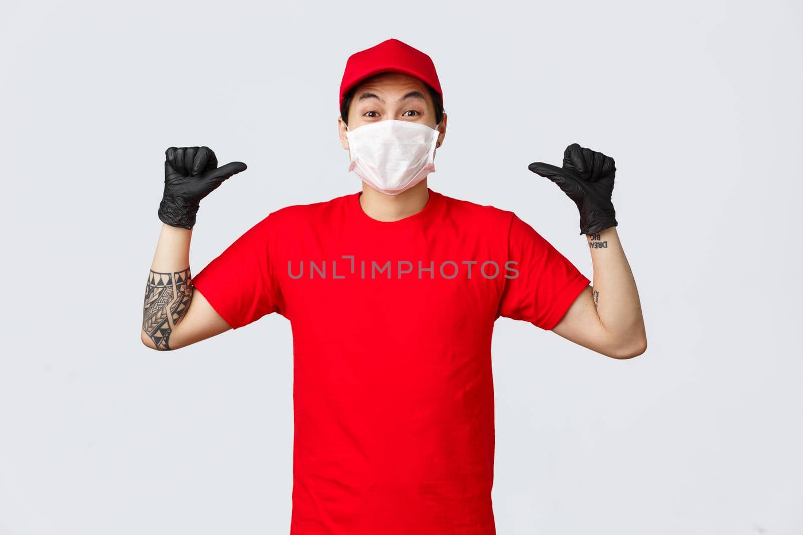 Cheerful, happy asian delivery guy in red cap and t-shirt, wearing protective gloves and medical mask, smiling eyes and pointing himself, got work in delivery company, become employee of year.