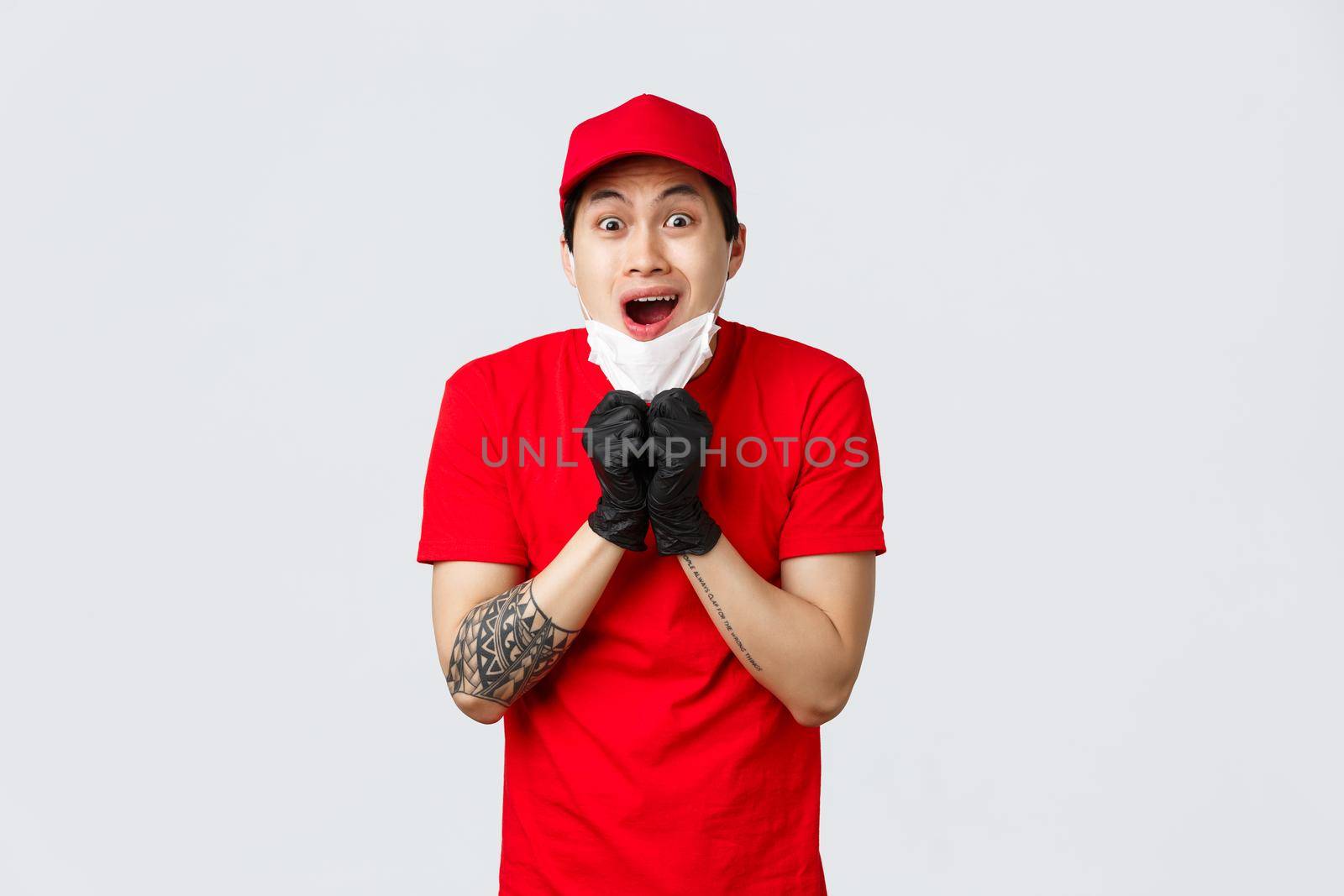 Freak out, shocked asian delivery guy gasping, drop jaw from amazement, take-off medical mask and staring with opened mouth camera. Courier in protective gloves excited looking you.