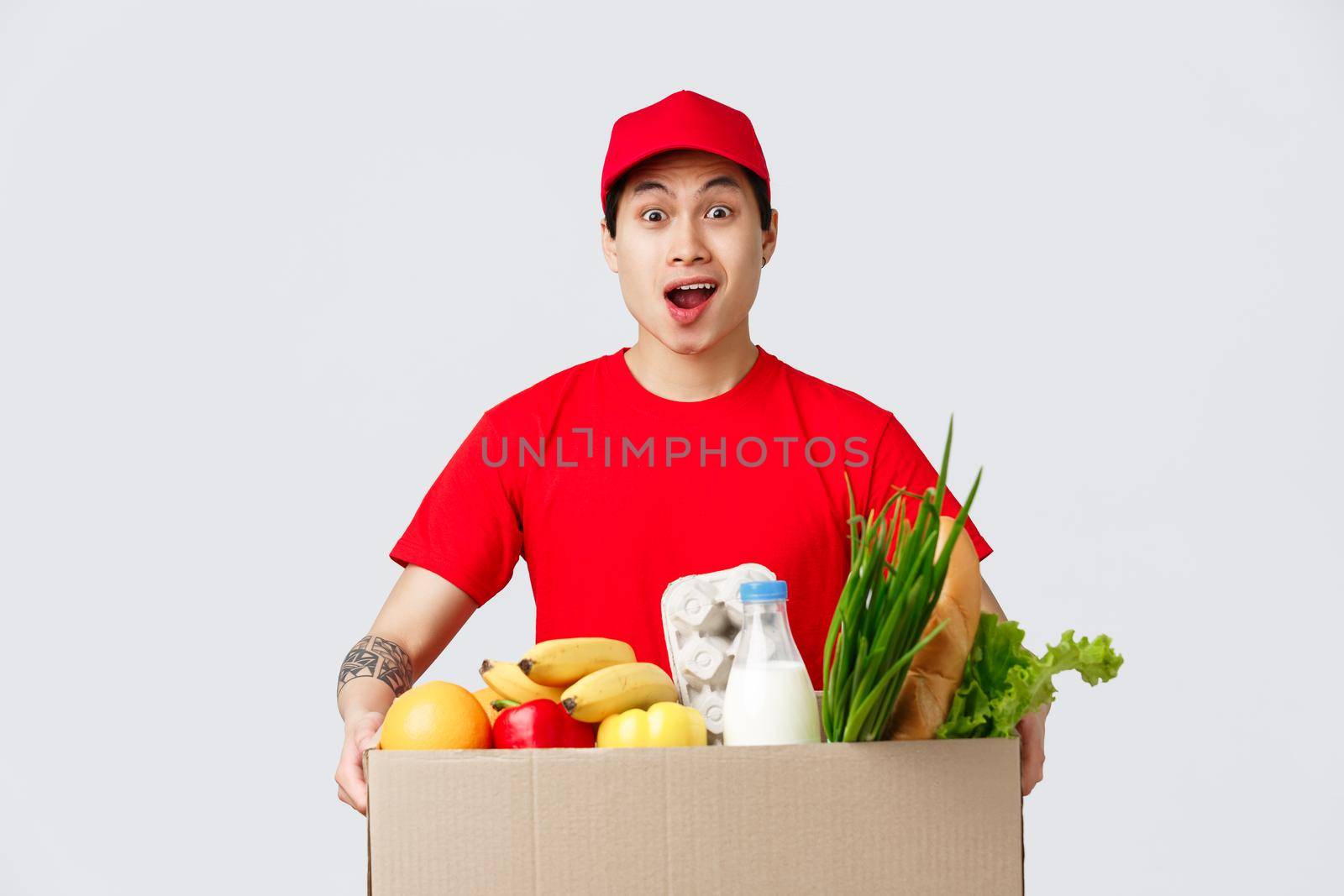 Online shopping, food delivery and internet stores concept. Shocked asian delivery guy carry huge box of client order, hold groceries product package, courier astonished.