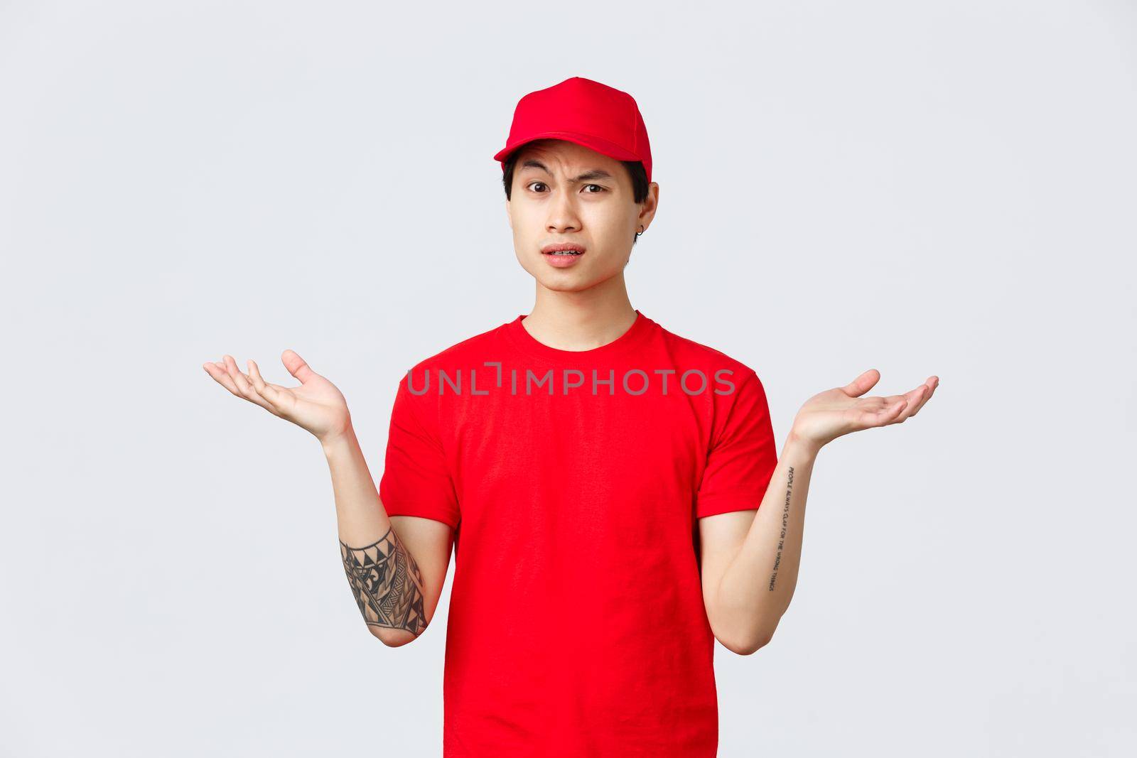 Express delivery, shipping and logistics concept. Courier dont understand why, wearing red cap and t-shirt, shrugging with hands spread sideways, grimacing bothered, complain.