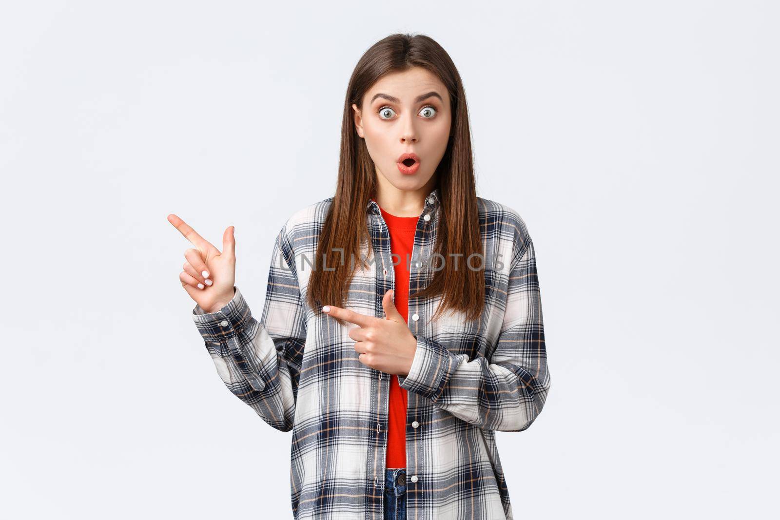 Lifestyle, different emotions, leisure activities concept. Impressed female customer, girl in casual checked shirt, say wow talking about news and pointing fingers left, white background.