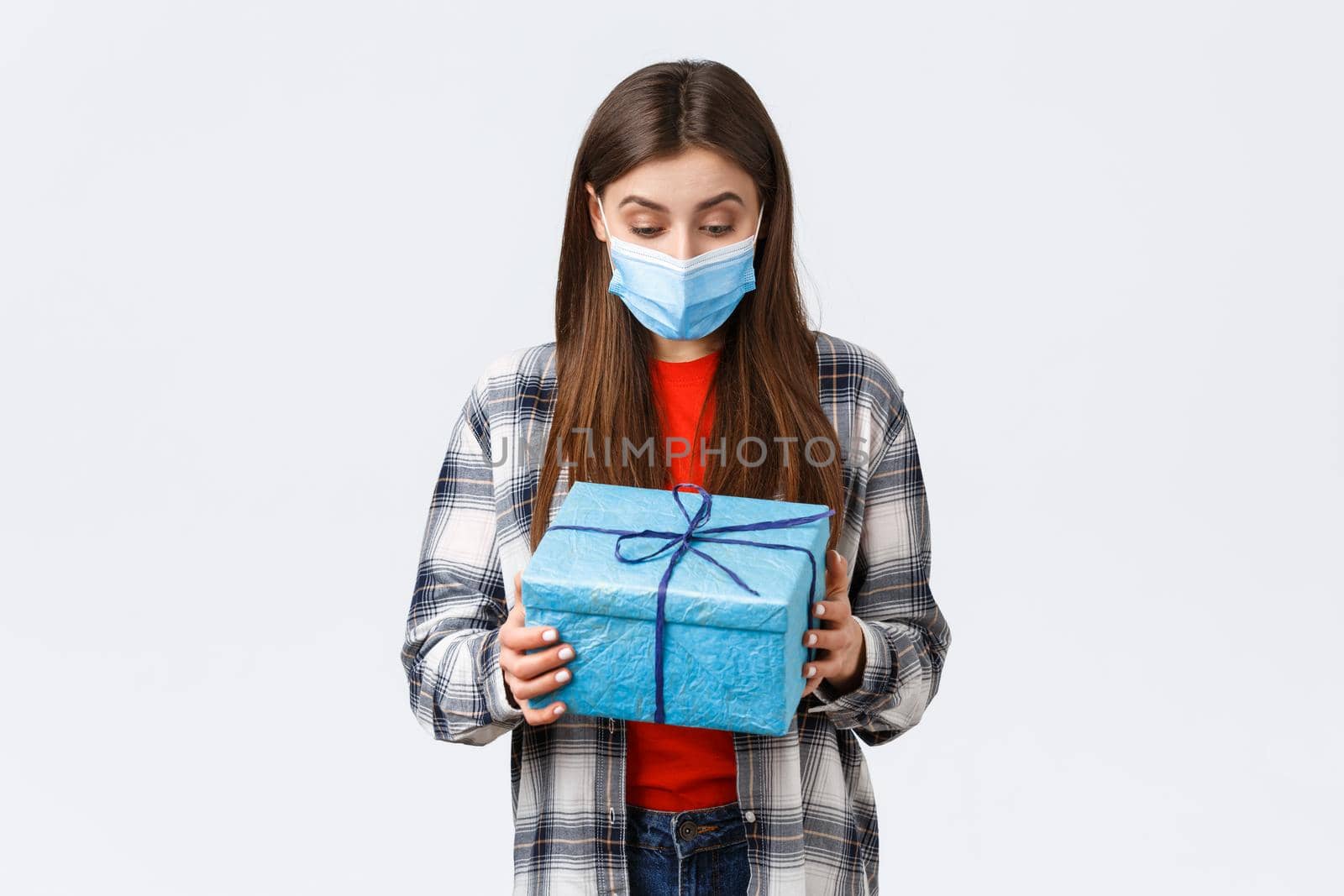 Covid-19, lifestyle, holidays and celebration concept. Happy and surprised birthday girl, employee receive present from coworkers, looking at wrapped gift with amazed grateful face in medical mask by Benzoix