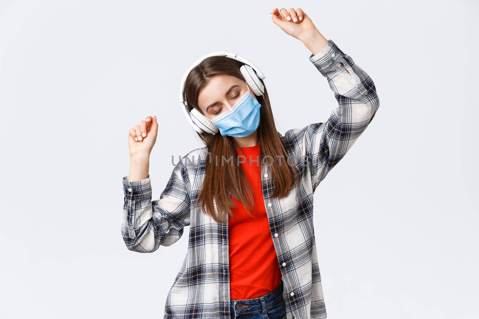 Social distancing, leisure and lifestyle on covid-19 outbreak, coronavirus concept. Carefree, relaxed good-looking woman in medical mask listening music in headphones, dancing with closed eyes.