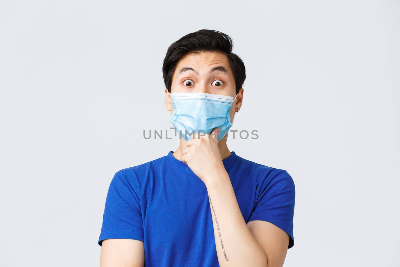 Different emotions, lifestyle and leisure during coronavirus, covid-19 concept. Close-up of intrigued asian guy listening to interesting suggestion, wear medical mask, touch chin and stare impressed.