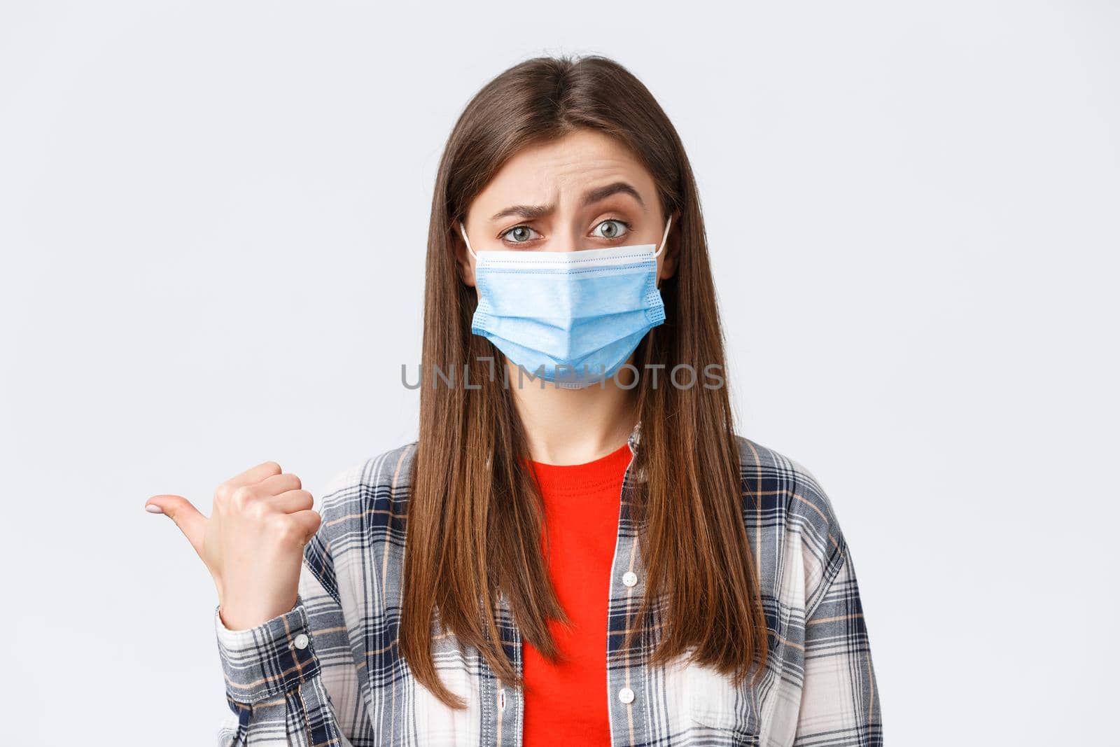 Coronavirus outbreak, leisure on quarantine, social distancing and emotions concept. Skeptical young woman in medical mask express disbelief towards banner to the left, pointing doubtful.