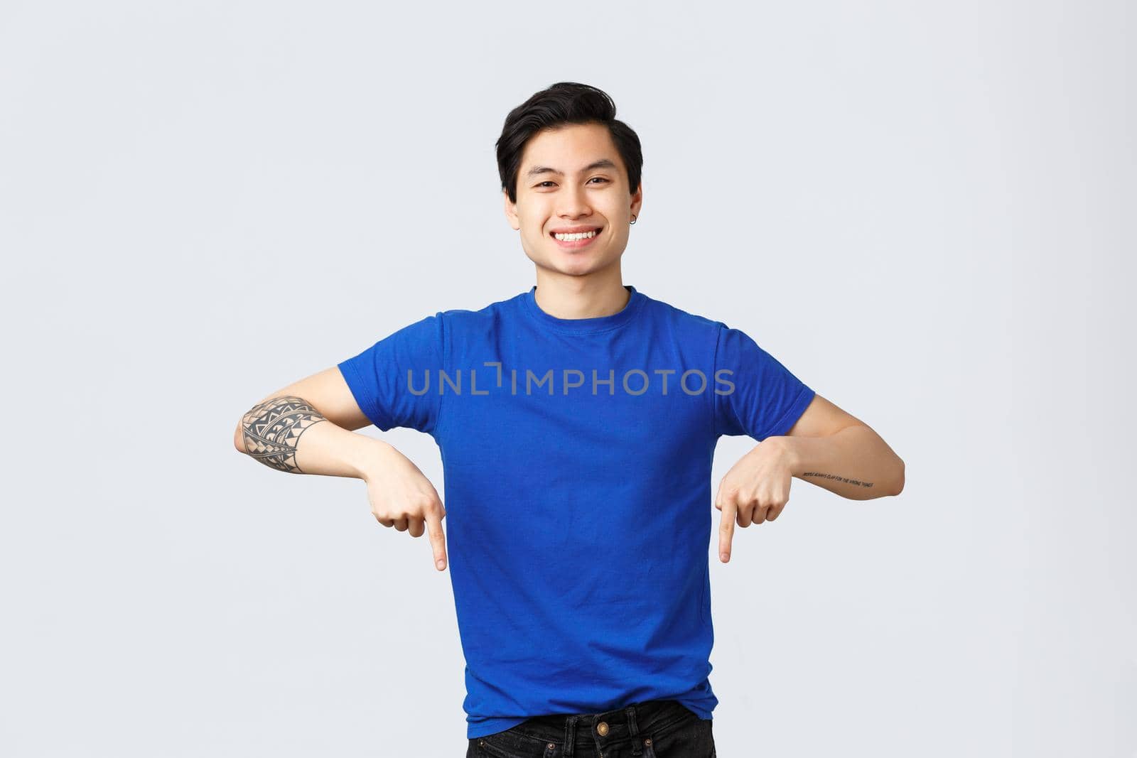Different emotions, people lifestyle and advertising concept. Handsome cheerful smiling asian man in blue t-shirt pointing fingers down. Attractive male student announce news, showing banner.