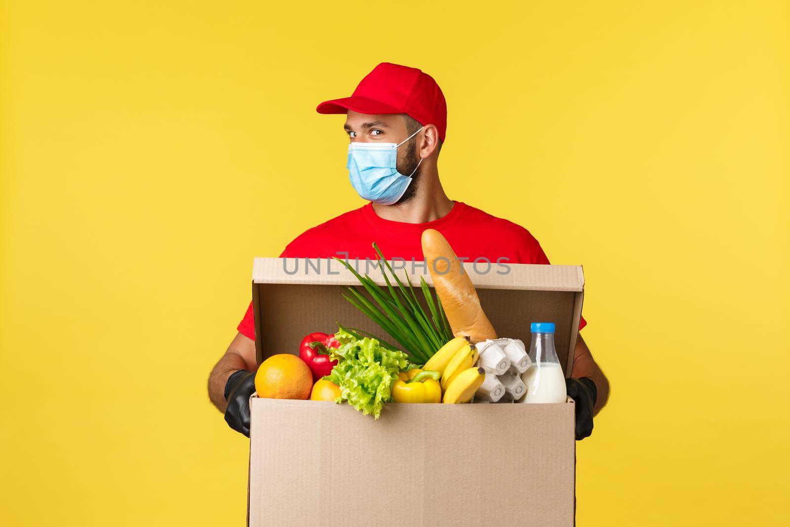 Takeaway delivery, covid-19 quarantine and groceries concept. Enthusiastic courier in red uniform, medical mask, look cheeky, bring customer food deliver, online order to doorstep.