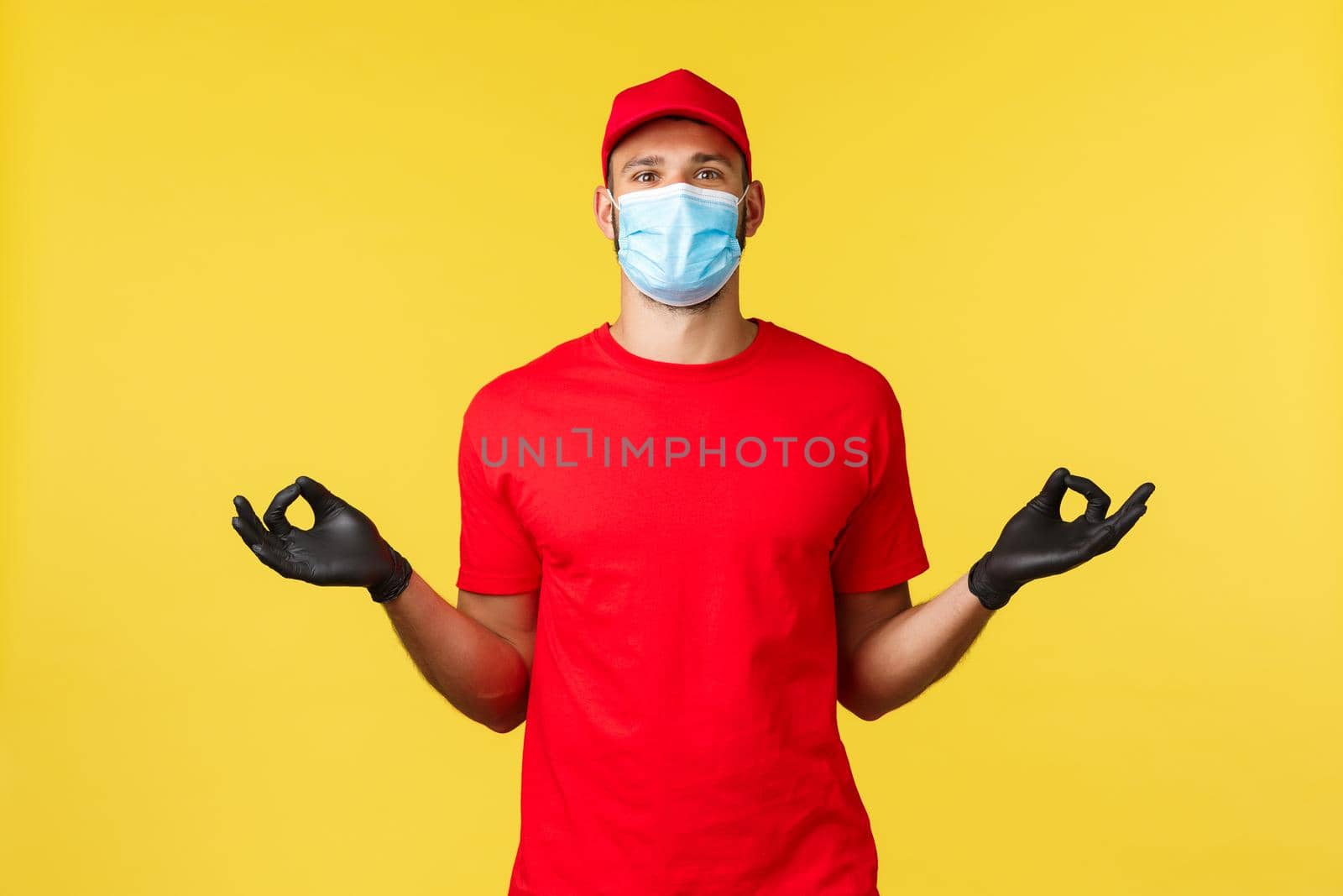 Express delivery during pandemic, covid-19, safe shipping, online shopping concept. Calm and peaceful courier in red uniform, medical mask and gloves, hold hands zen, meditating, yellow background.