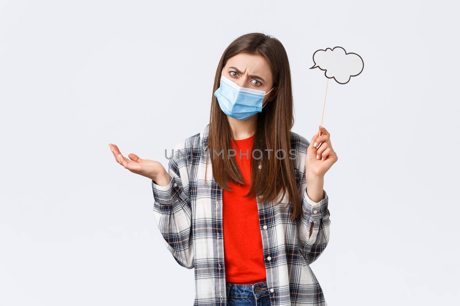 Coronavirus outbreak, leisure on quarantine, social distancing and emotions concept. Girl with bubble thought cloud looking confused, dont understand, shrugging and wear medical mask.