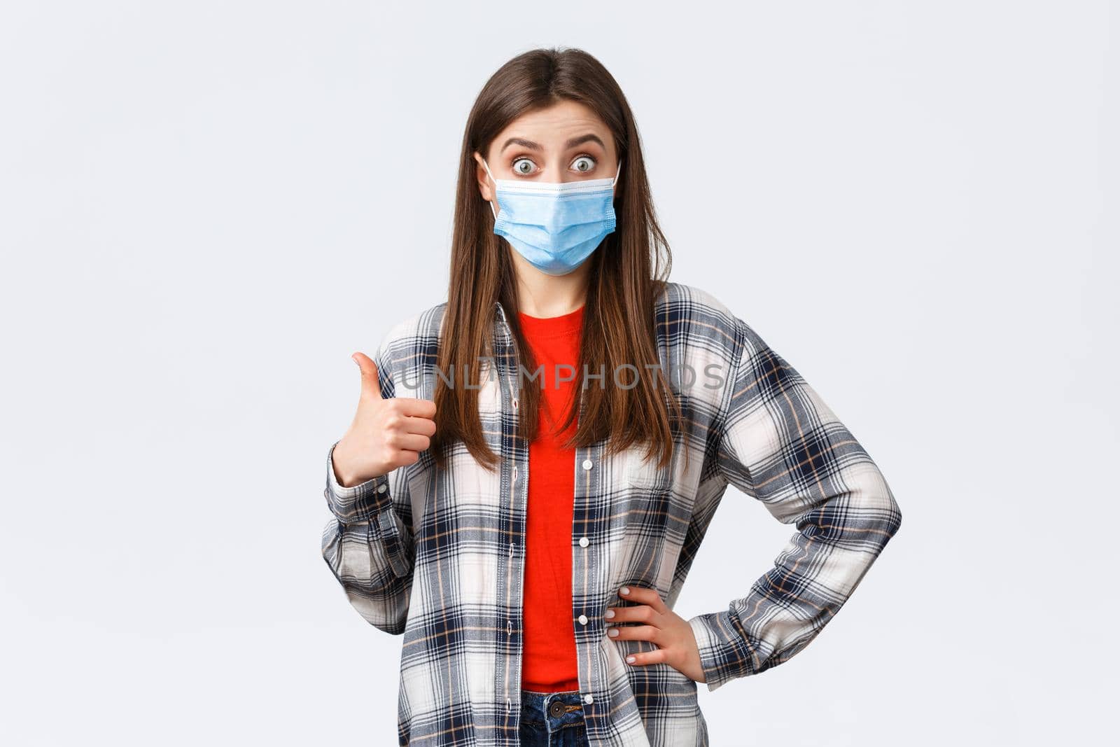 Coronavirus outbreak, leisure on quarantine, social distancing and emotions concept. Excited and surprised young woman in medical mask hear really good idea, show thumb-up in approval by Benzoix