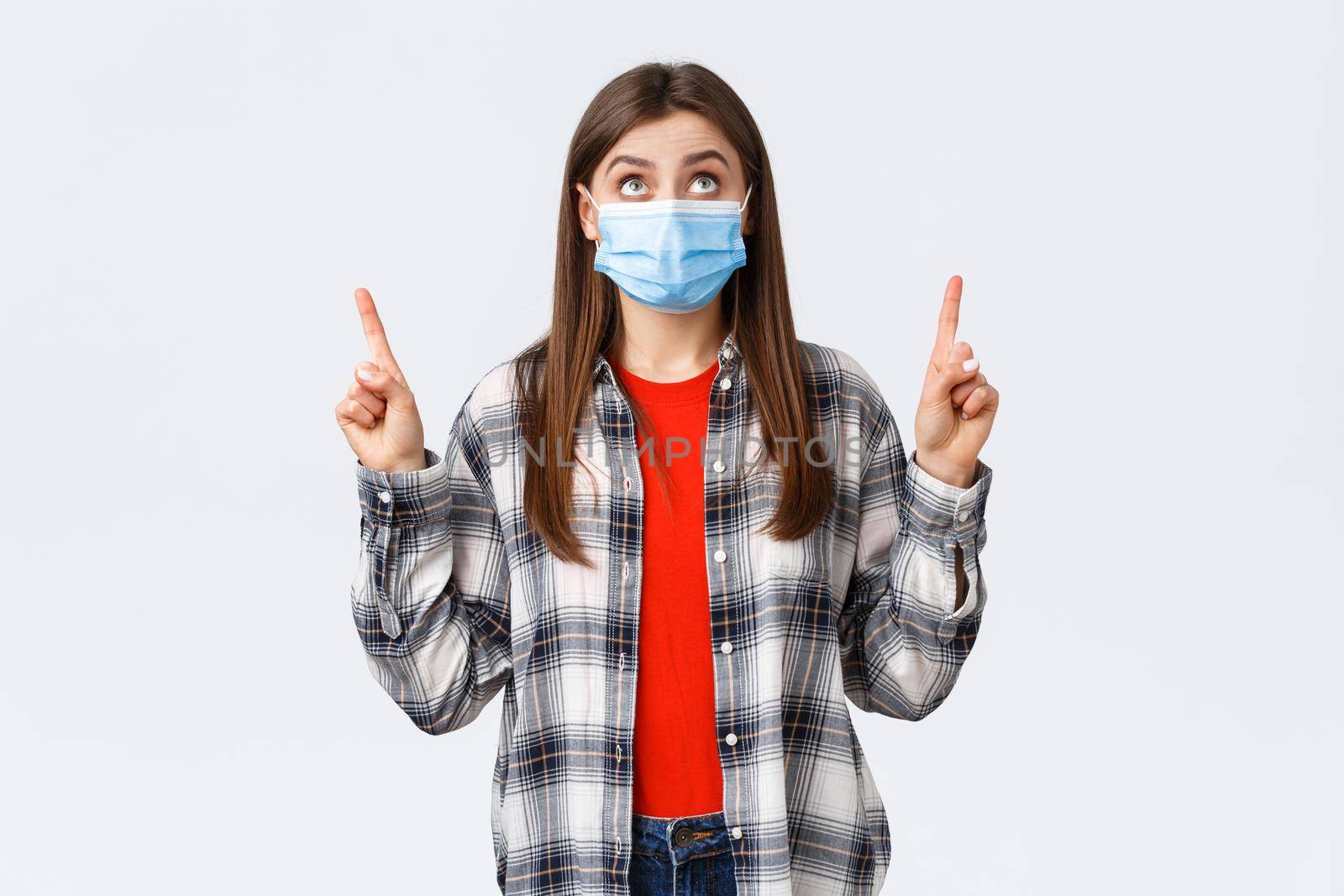 Coronavirus outbreak, leisure on quarantine, social distancing and emotions concept. Surprised and interested cute caucasian girl in casual outfit and medical mask, reading sign upwards, point up.