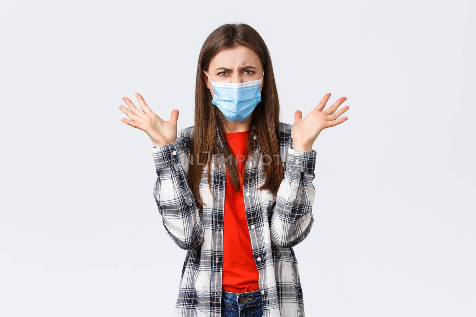 Different emotions, covid-19 pandemic, coronavirus self-quarantine and social distancing concept. Angry, outraged woman in medical mask, arguing, look mad, raise hands in dismay, complaining by Benzoix