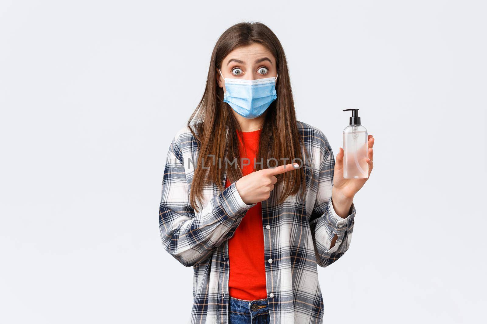 Coronavirus outbreak, leisure on quarantine, social distancing and emotions concept. Excited and astonished young woman in medical mask, pointing at hand sanitizer, recommend product.