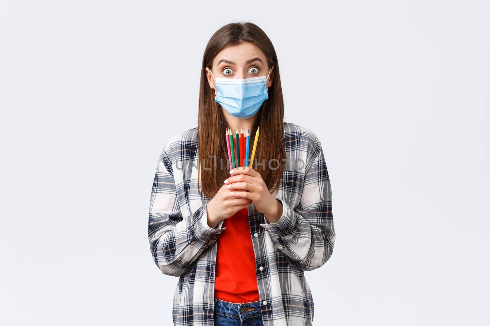 Social distancing, leisure and hobbies on covid-19 outbreak, coronavirus concept. Enthusiastic cute girl in medical mask trying new thing on self-quarantine, showing colored pencils, learn how draw by Benzoix