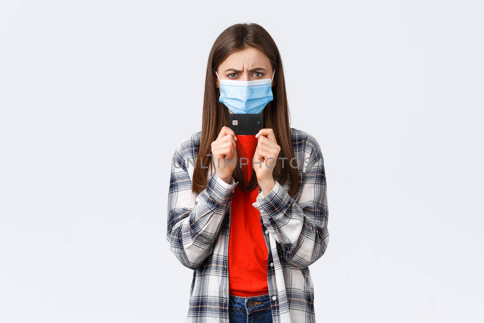 Coronavirus outbreak, working from home, online shopping and contactless payment concept. Angry or frustrated young woman in medical mask frowning displeased, holding credit card by Benzoix