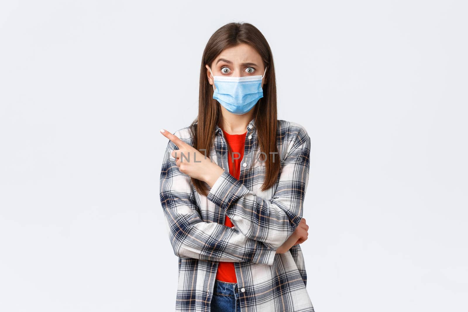 Coronavirus outbreak, leisure on quarantine, social distancing and emotions concept. Confused and worried girl asking question about smth strange, pointing finger left, wear medical mask covid-19.