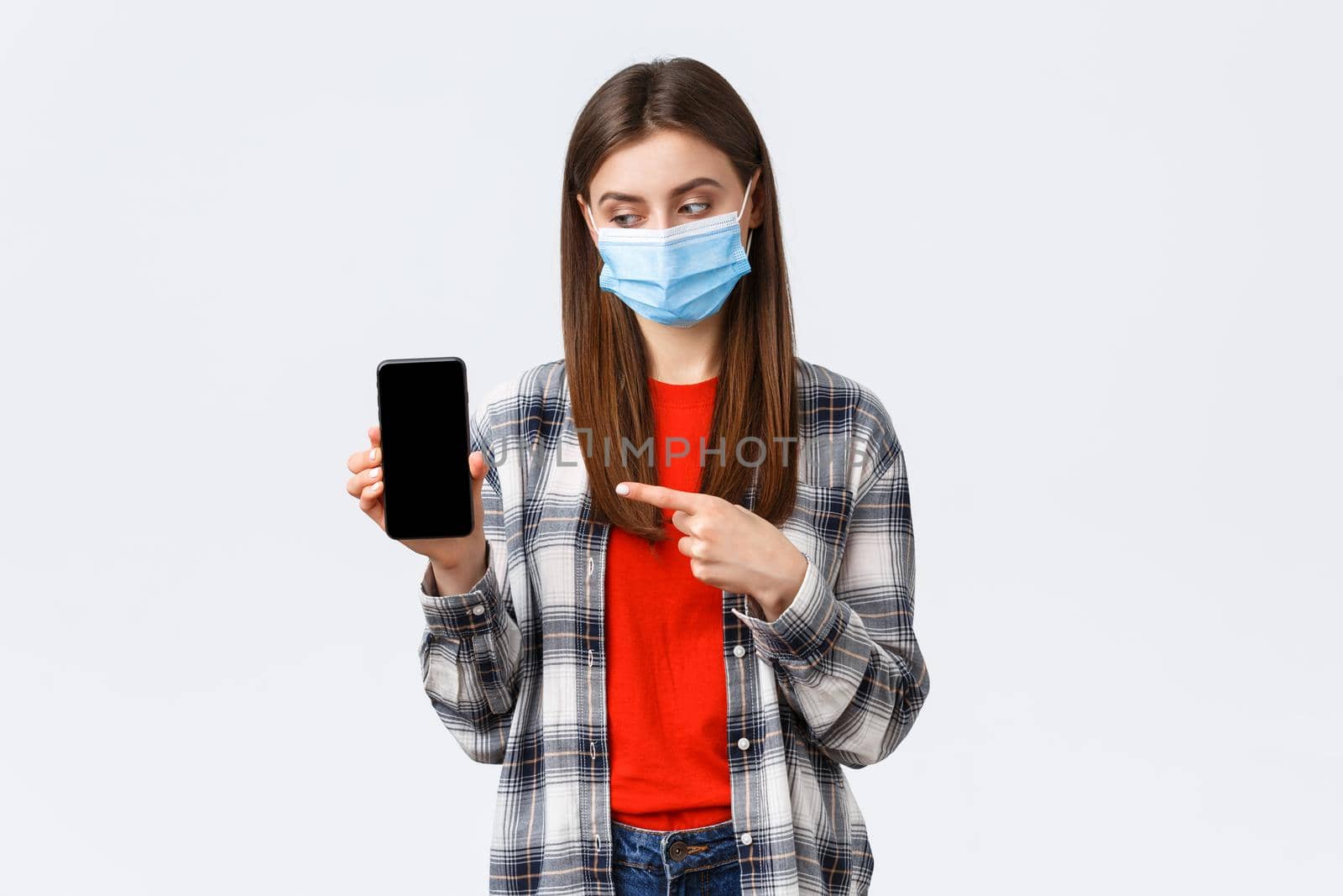 Different emotions, covid-19, social distancing and technology concept. Attractive 20s female in medical mask, pointing finger at mobile phone, advice download app or game, filters for photos by Benzoix