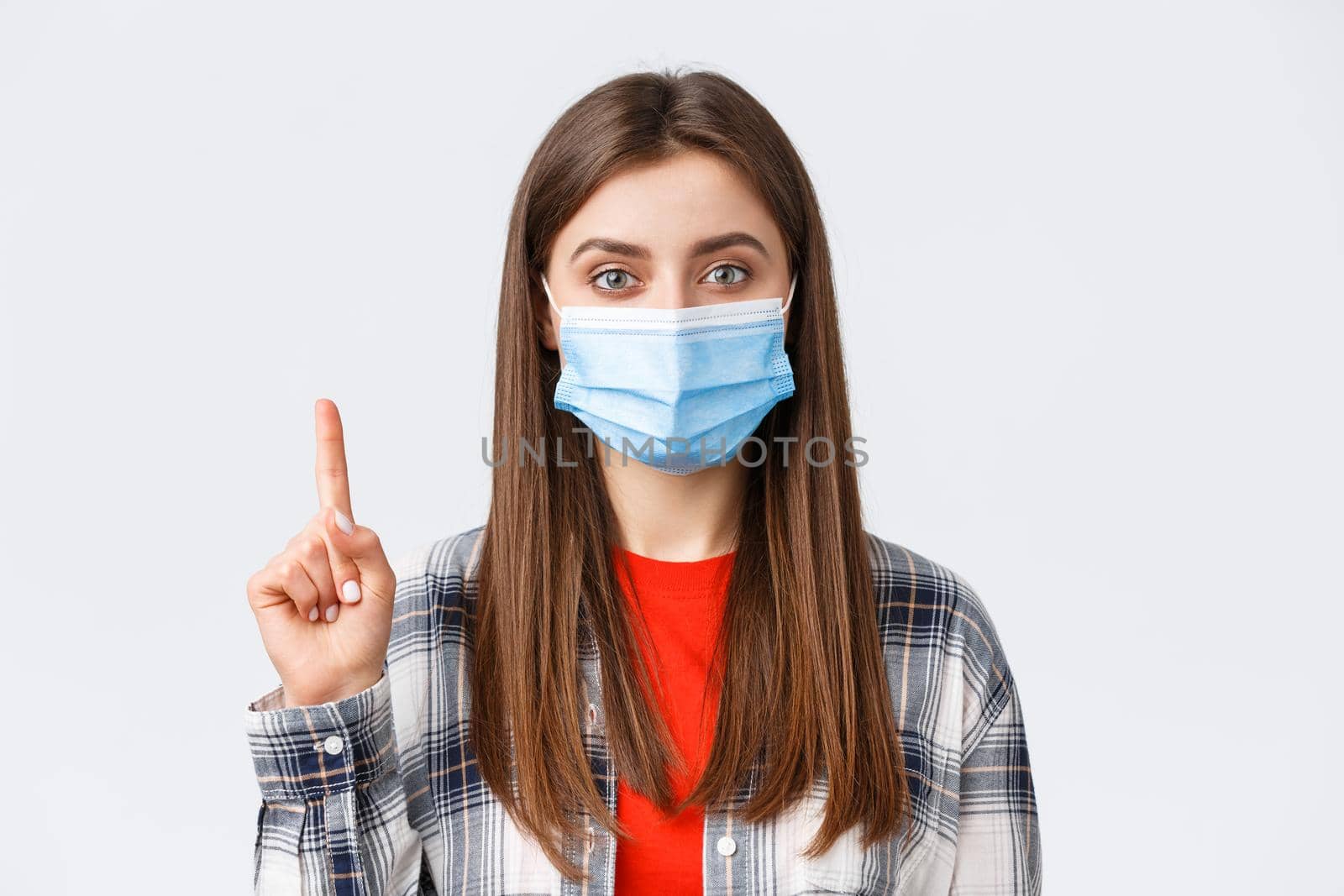Coronavirus outbreak, leisure on quarantine, social distancing and emotions concept. Close-up of cute young woman in medical mask explain smth, show number one or point up.