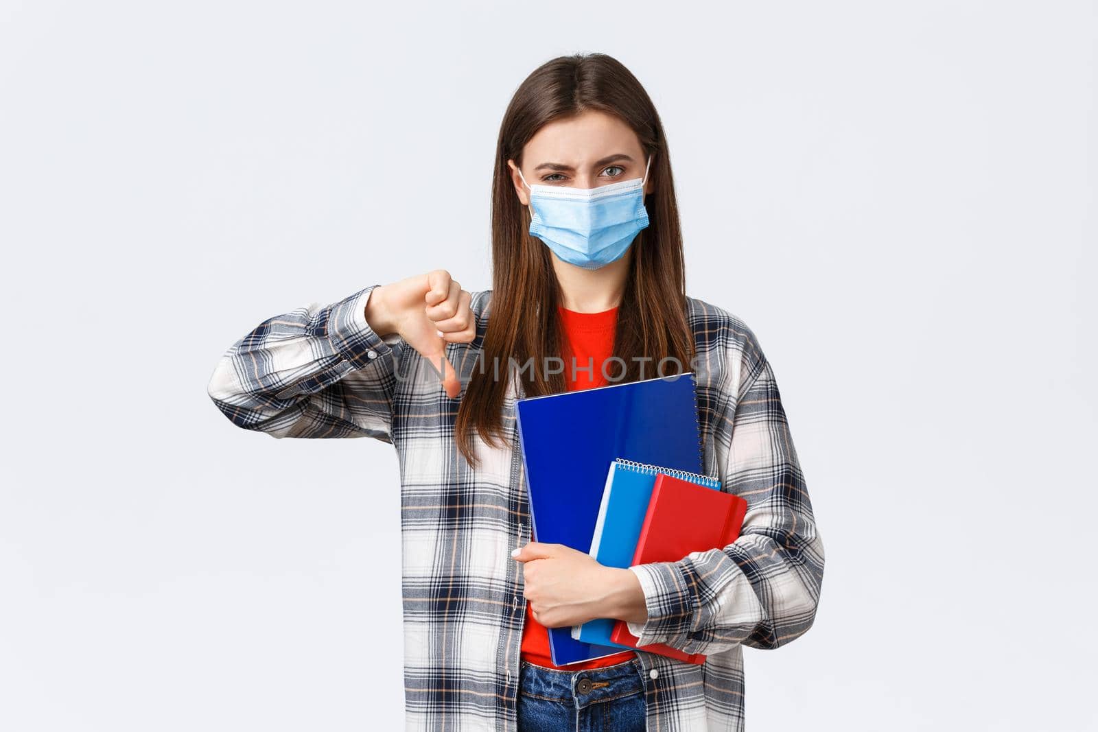 Coronavirus pandemic, covid-19 education, and back to school concept. Displeased and disappointed female student, freshman in medical mask thumb-down and grimacing discussing smth bad.