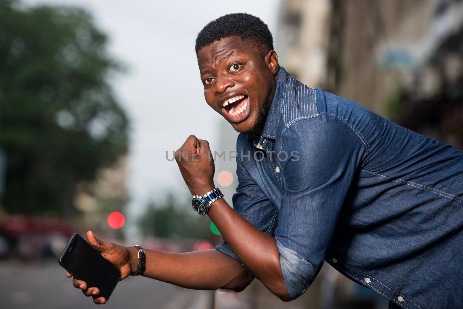 young man in jeans with elbows on iron bar looking at camera laughing.