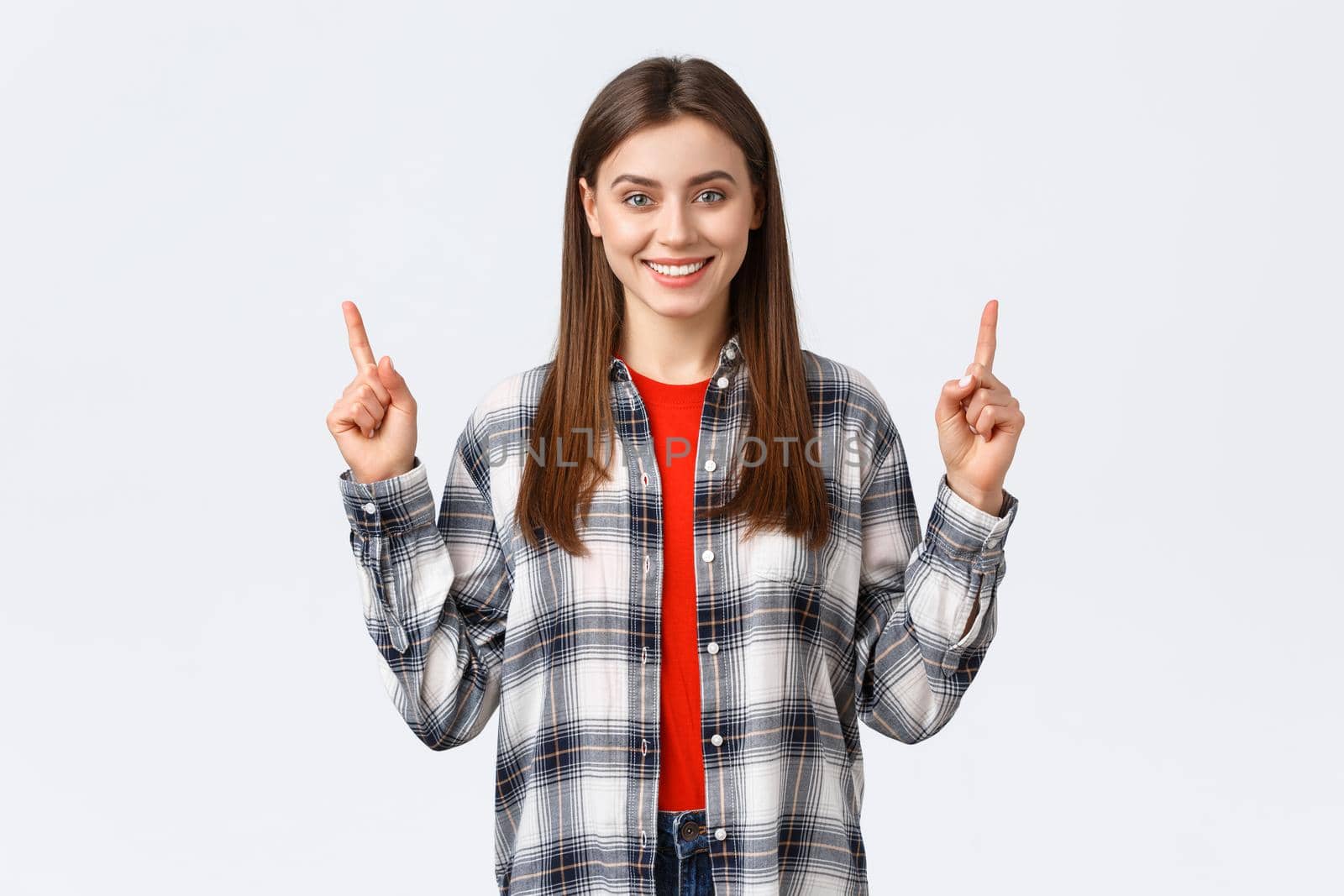 Lifestyle, different emotions, leisure activities concept. Confident smiling girl in checked shirt, turn attention to upper banner, pointing fingers up and look camera, telling about advertisement.