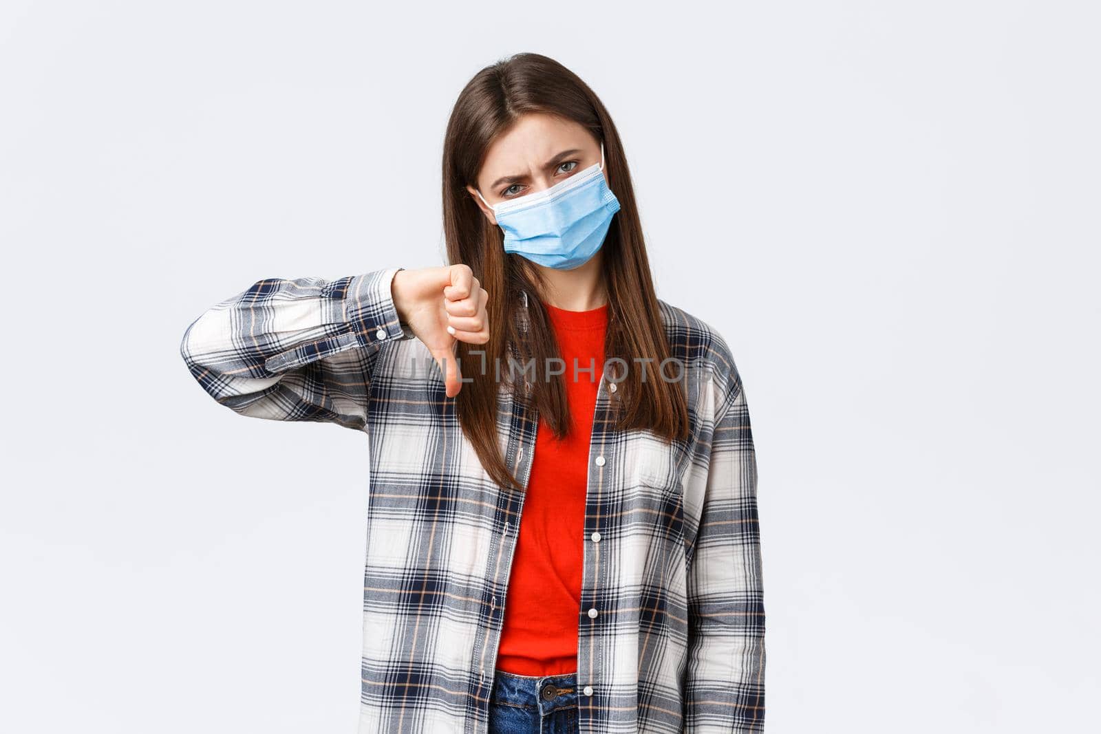 Coronavirus outbreak, leisure on quarantine, social distancing and emotions concept. Lame bad idea. Displeased and unamused young woman in medical mask thumb-down in disapproval.