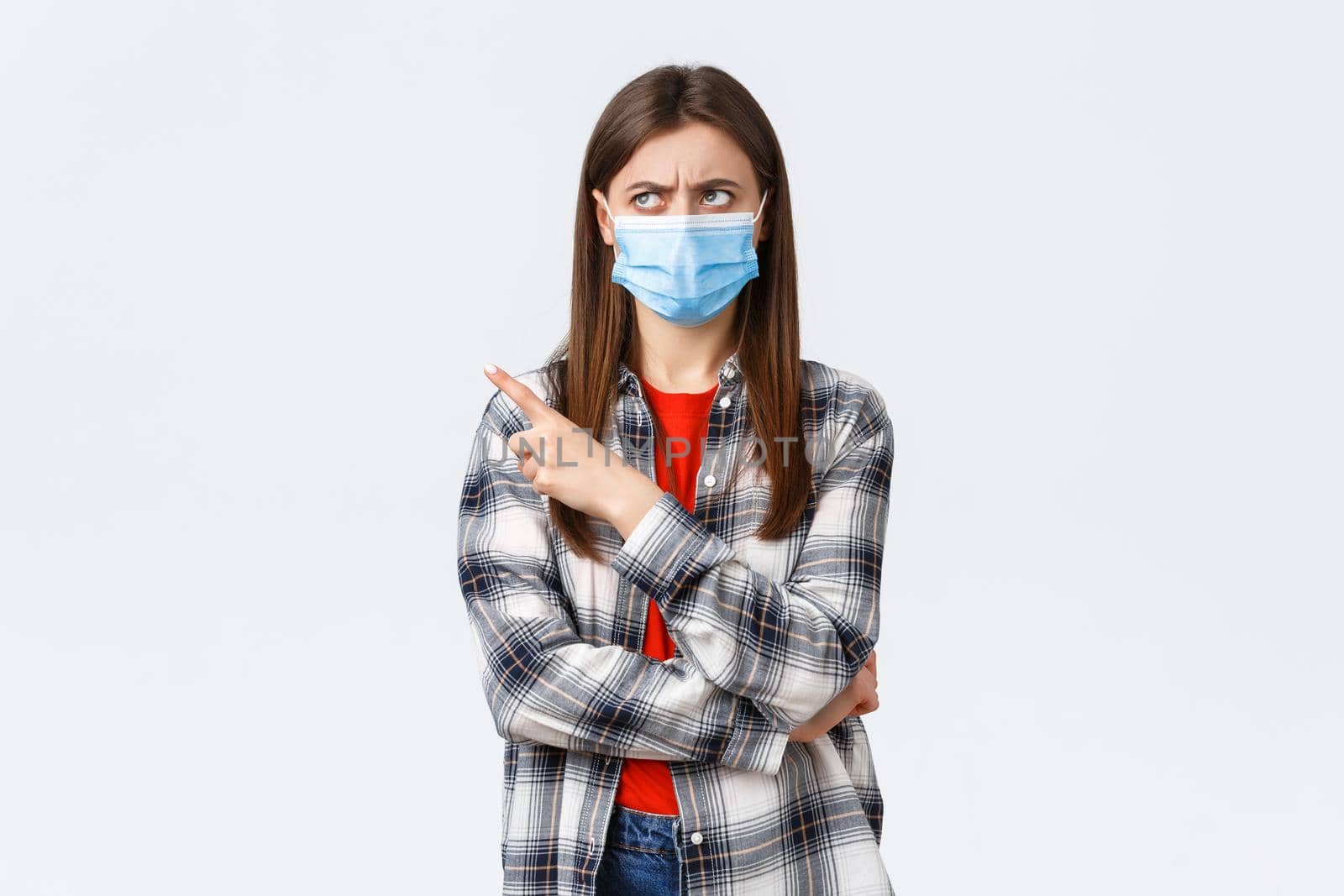 Coronavirus outbreak, leisure on quarantine, social distancing and emotions concept. Skeptical young girl express disbelief, frowning, looking and pointing upper left corner, wear medical mask.