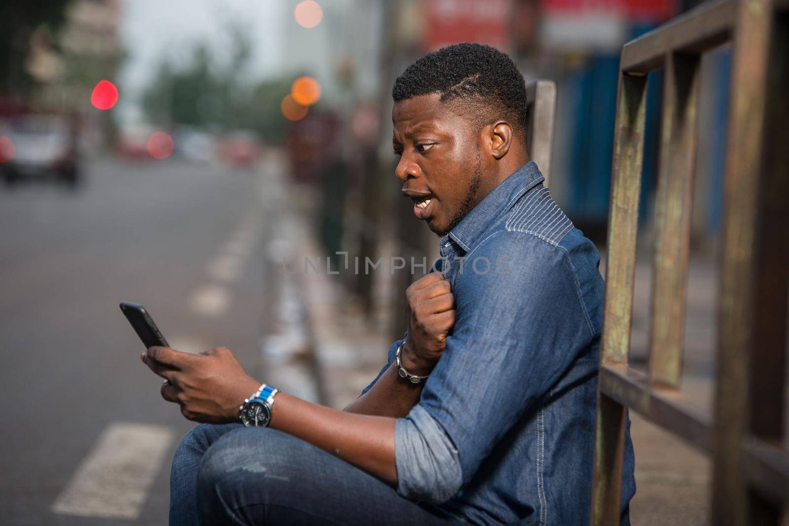 young man sitting in jeans near bar looking at mobile phone with surprise.