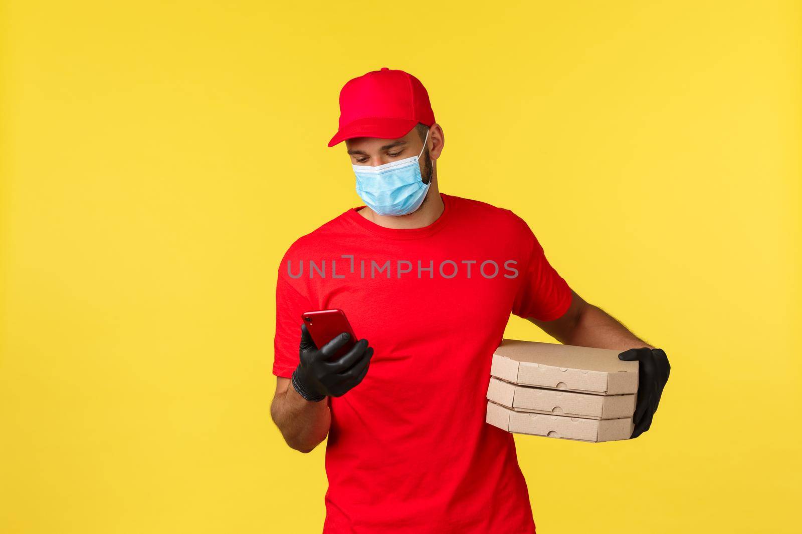 Food delivery, tracking orders, covid-19 and self-quarantine concept. Courier checking client adress on phone as bring pizza order, calling customer, standing yellow background.