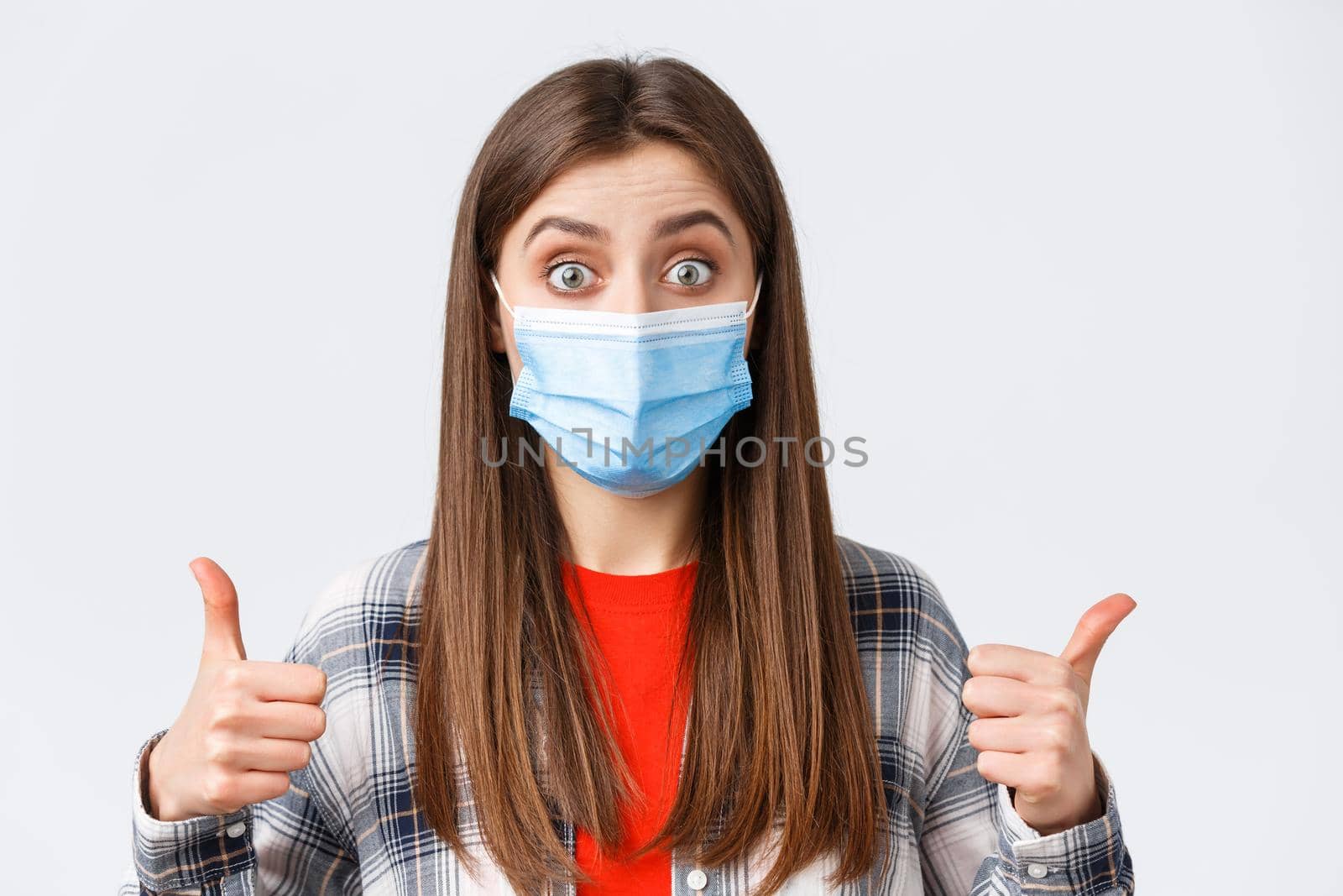 Coronavirus outbreak, leisure on quarantine, social distancing and emotions concept. Sounds good. Excited and pleased, satisfied female in medical mask, show thumb-up, interesting idea.