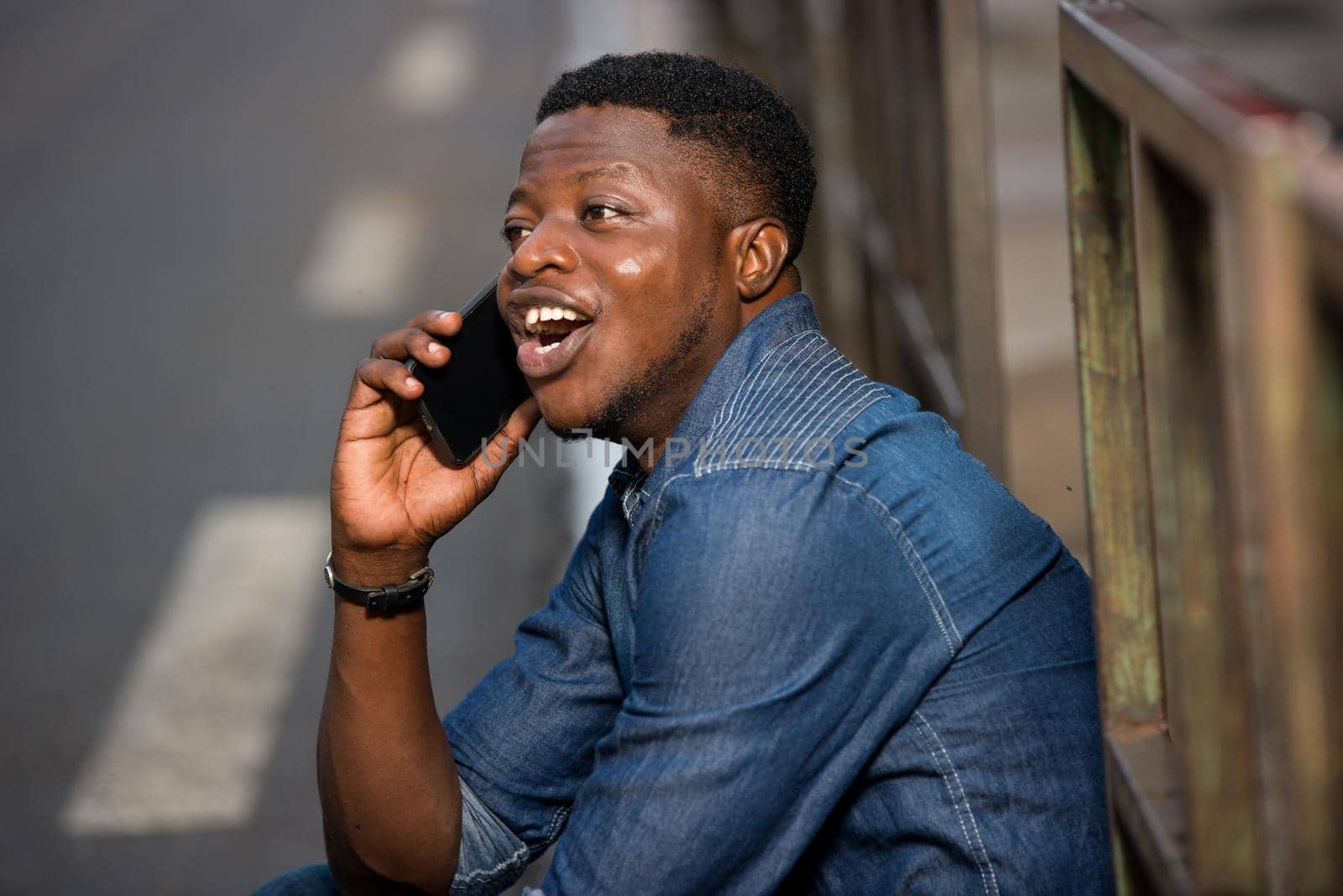 young man sitting in jeans near iron bar talking on mobile phone laughing.