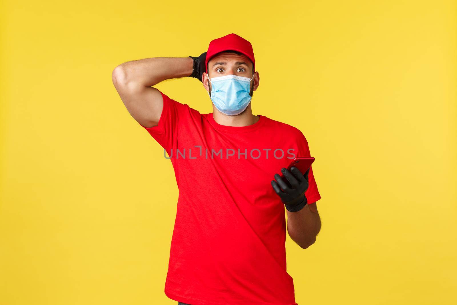 Food delivery, tracking orders, covid-19 and self-quarantine concept. Worried newbie courier first day at work, trying call client, using smartphone app, look nervous, touch head and look camera.