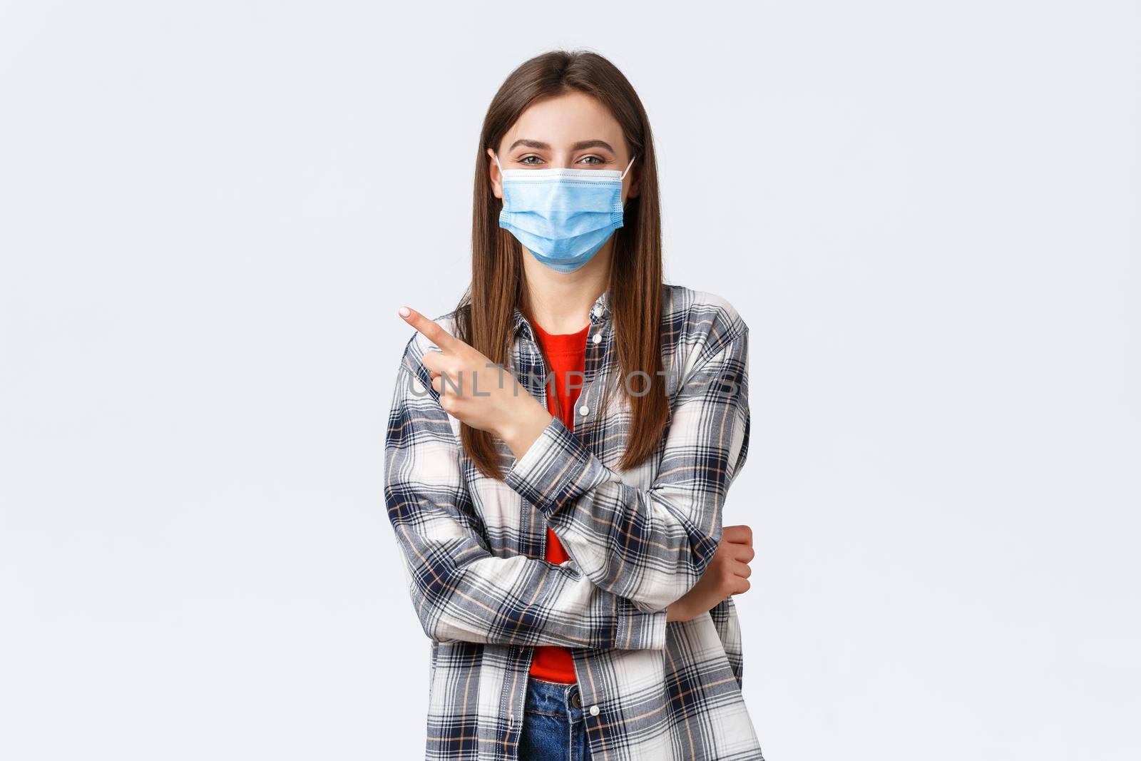 Coronavirus outbreak, leisure on quarantine, social distancing and emotions concept. Cheerful smiling caucasian woman in medical mask, pointing finger upper left corner, recommend link or product.