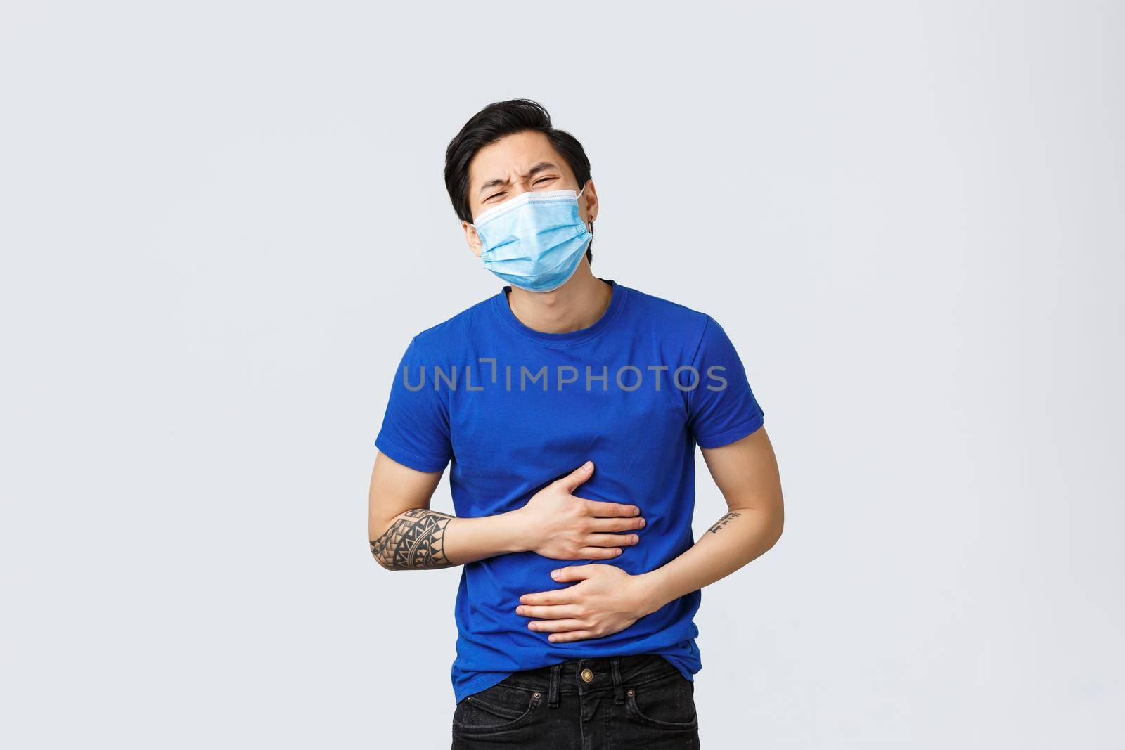 Different emotions, social distancing, self-quarantine and lifestyle concept. Asian guy suffering huge pain in stomach. Man with stomachache touching belly and bending from ache, food poison by Benzoix