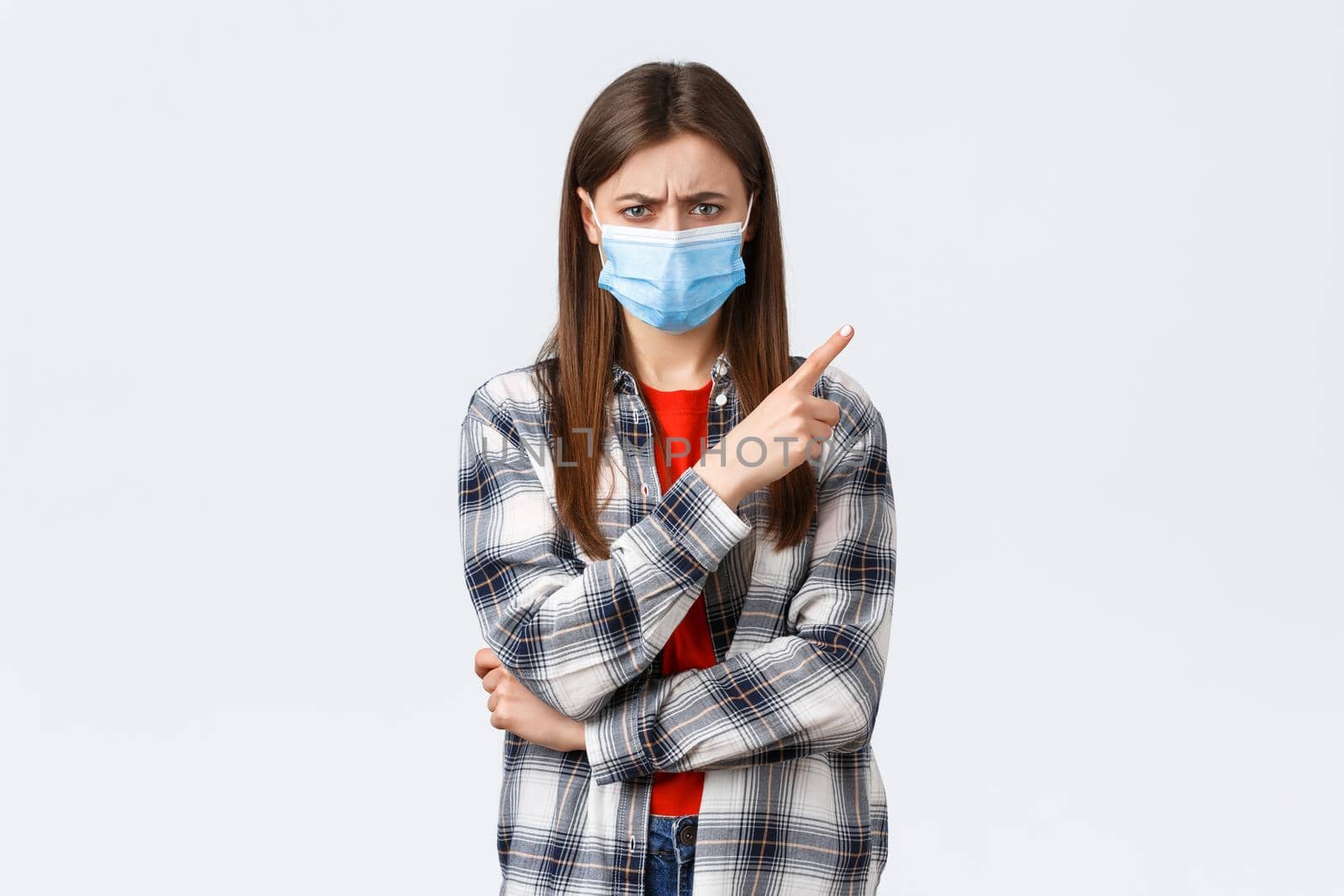 Coronavirus outbreak, leisure on quarantine, social distancing and emotions concept. Angry and disappointed, confused young woman pointing finger upper right corner frowning upset, wear mask.