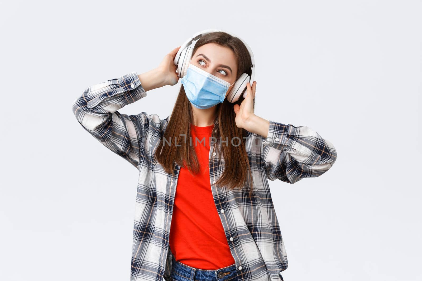 Social distancing, leisure and lifestyle on covid-19 outbreak, coronavirus concept. Happy carefree attractive girl in medical mask, look away dreamy, imaging while listening music in headphones.