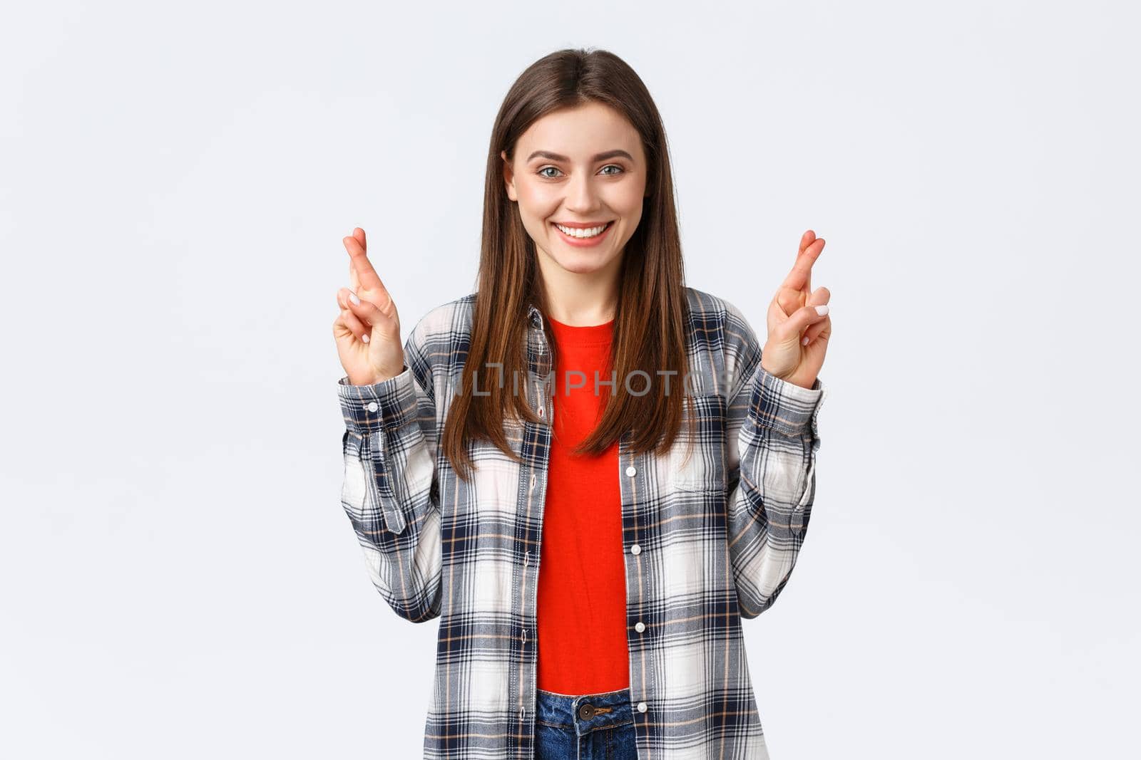 Lifestyle, different emotions, leisure activities concept. Hopeful cute caucasian girl in checked shirt, making wish, cross fingers good luck and smiling optimistic, white background.