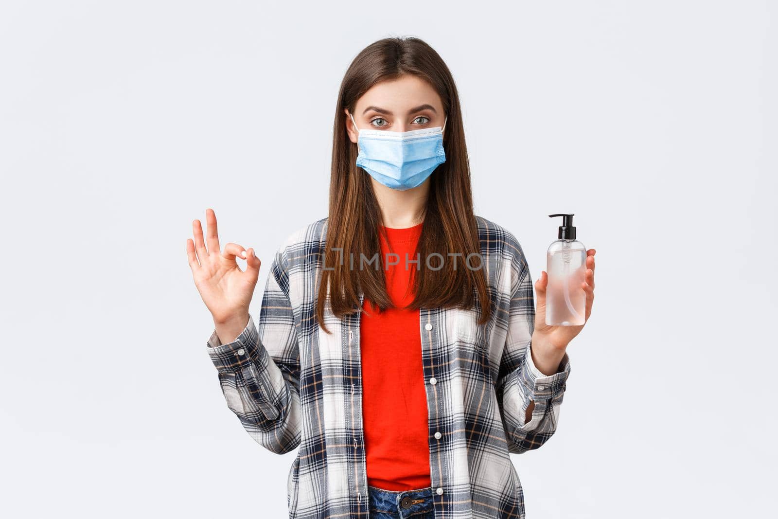 Coronavirus outbreak, leisure on quarantine, social distancing and emotions concept. Pleased assured young woman in medical mask recommend buy this hand sanitizer brand, show okay sign by Benzoix