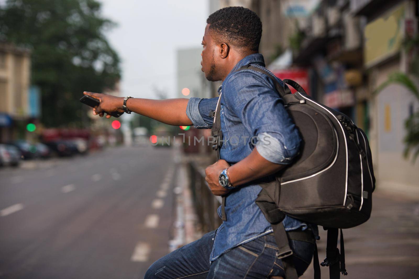 young man sitting on iron bar with backpack mobile phone in hand showing something finger