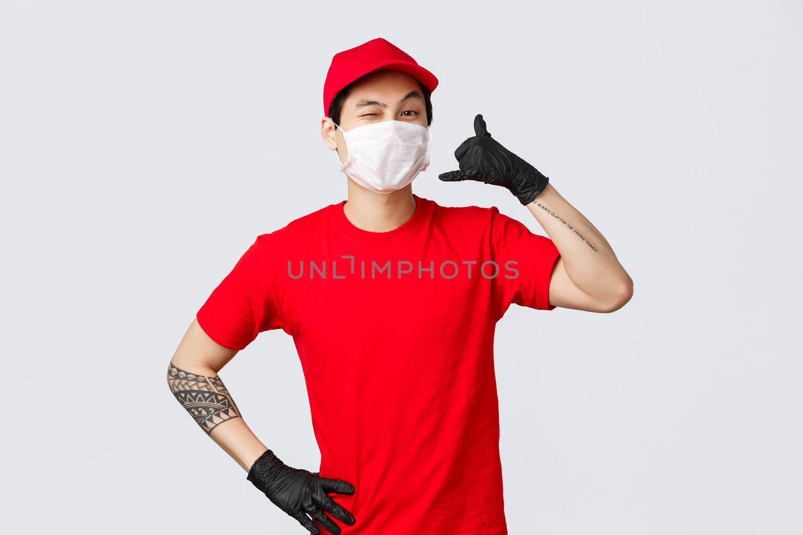 Happy asian delivery guy in medical mask tell give call, wink cheeky to client, keep in touch when delivery needed, fast shipment, good quality of courier services, safe shopping during pandemic.