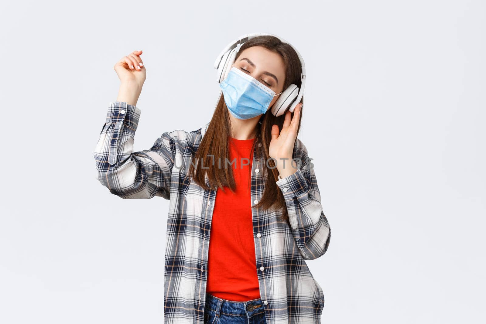 Social distancing, leisure and lifestyle on covid-19 outbreak, coronavirus concept. Carefree tender young woman carried away listening music in headphones, dancing with closed eyes in medical mask.