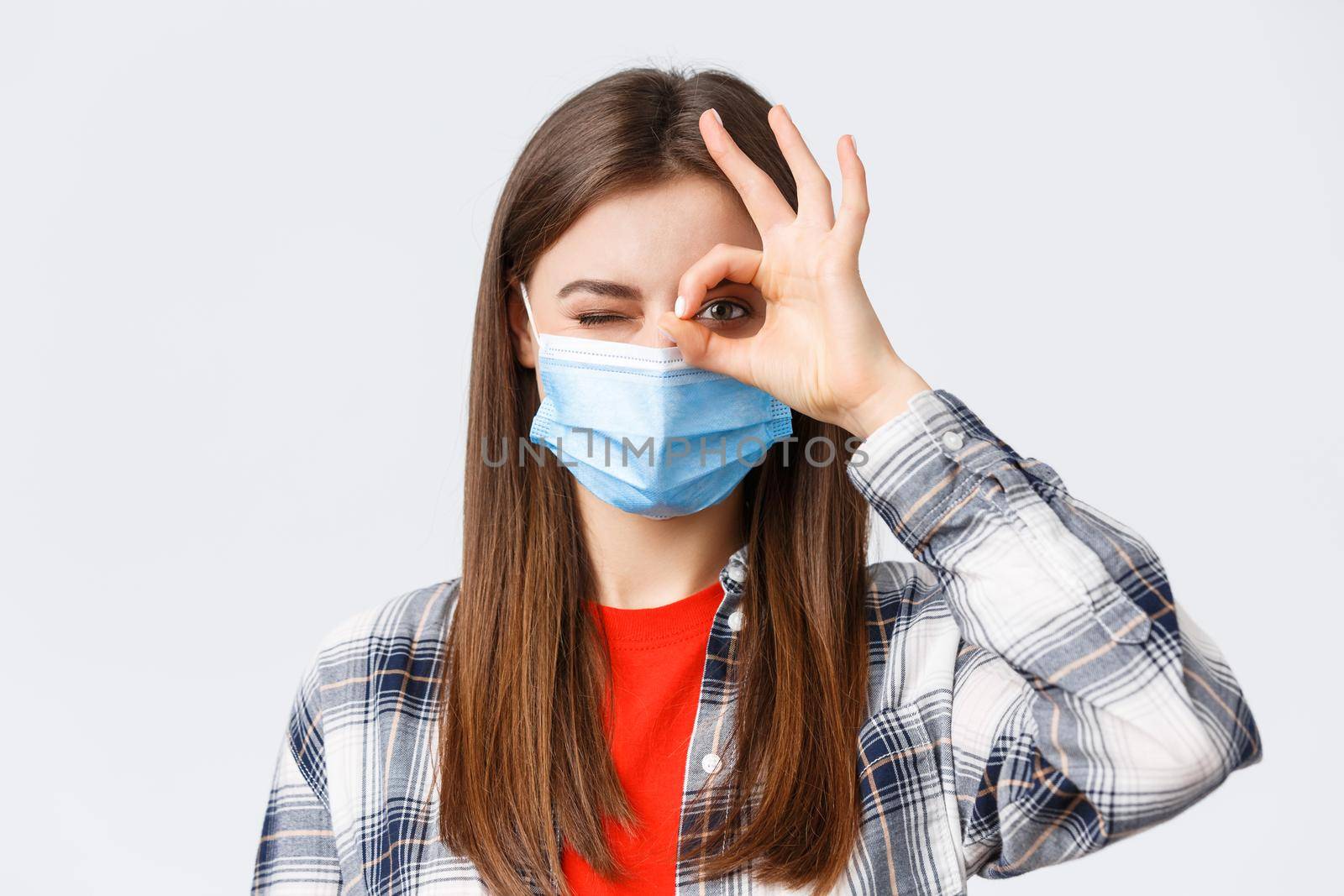 Coronavirus outbreak, leisure on quarantine, social distancing and emotions concept. Close-up of optimistic good-looking woman in medical mask show okay sign and wink.