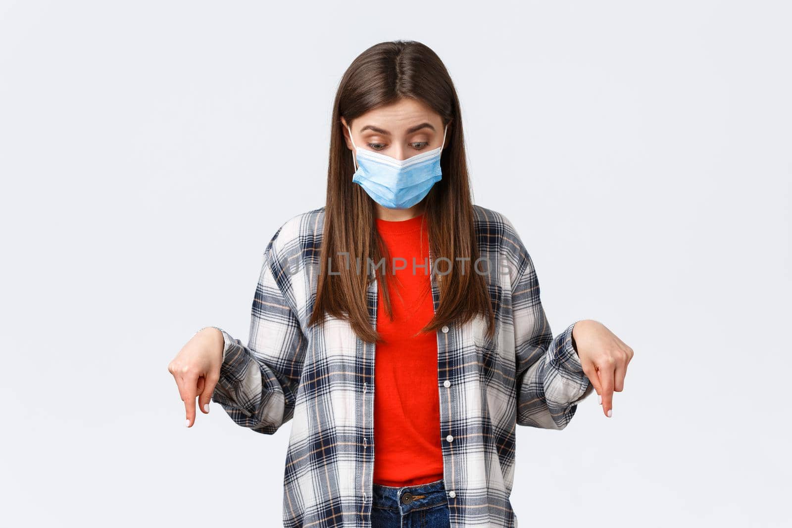 Coronavirus outbreak, leisure on quarantine, social distancing and emotions concept. Intrigued cute girl in medical mask. Woman wearing PPE from virus infection, looking pointing down.