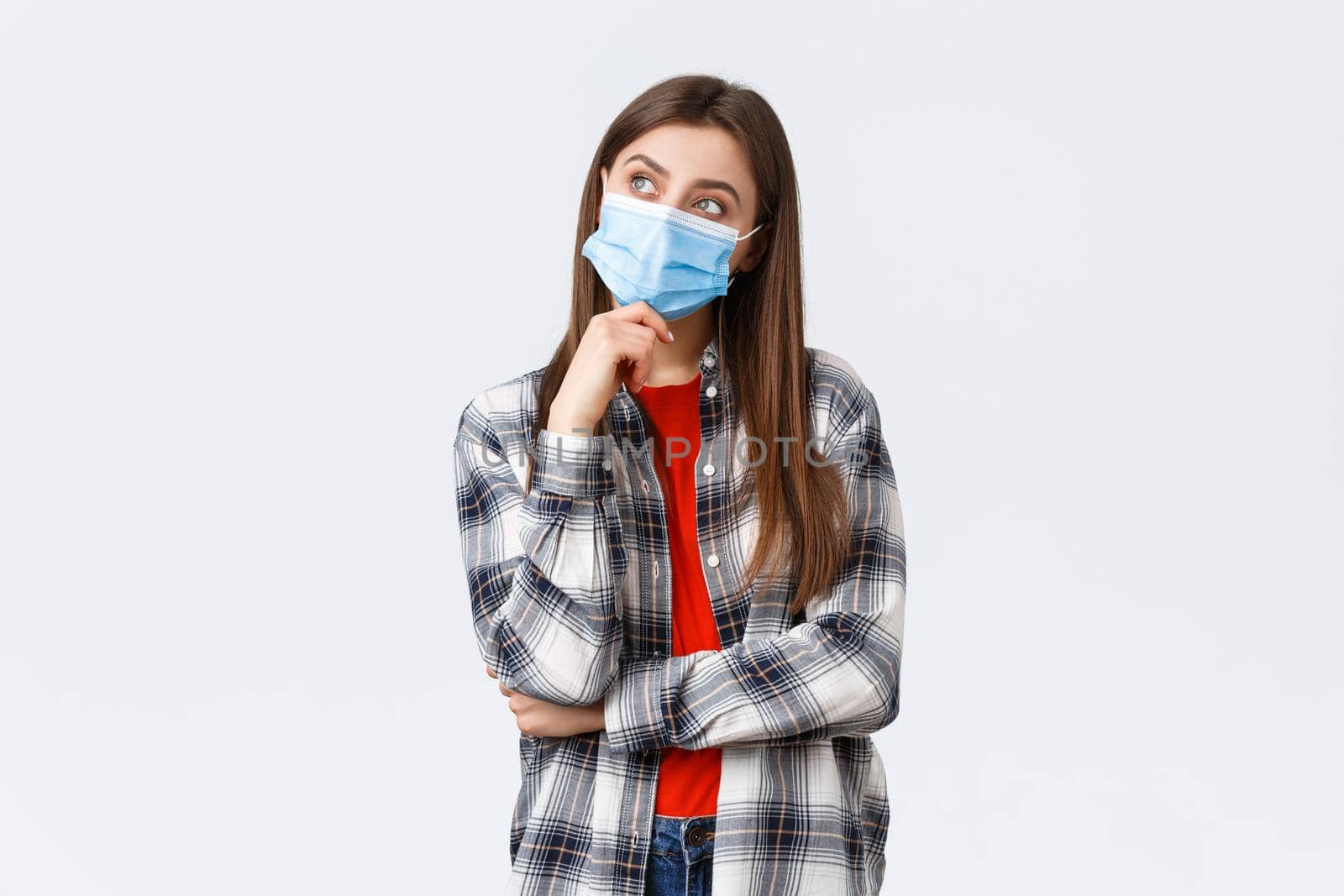 Coronavirus outbreak, leisure on quarantine, social distancing and emotions concept. Dreamy and thoughtful beautiful girl in medical mask, imaging something, thinking as look upper left corner.