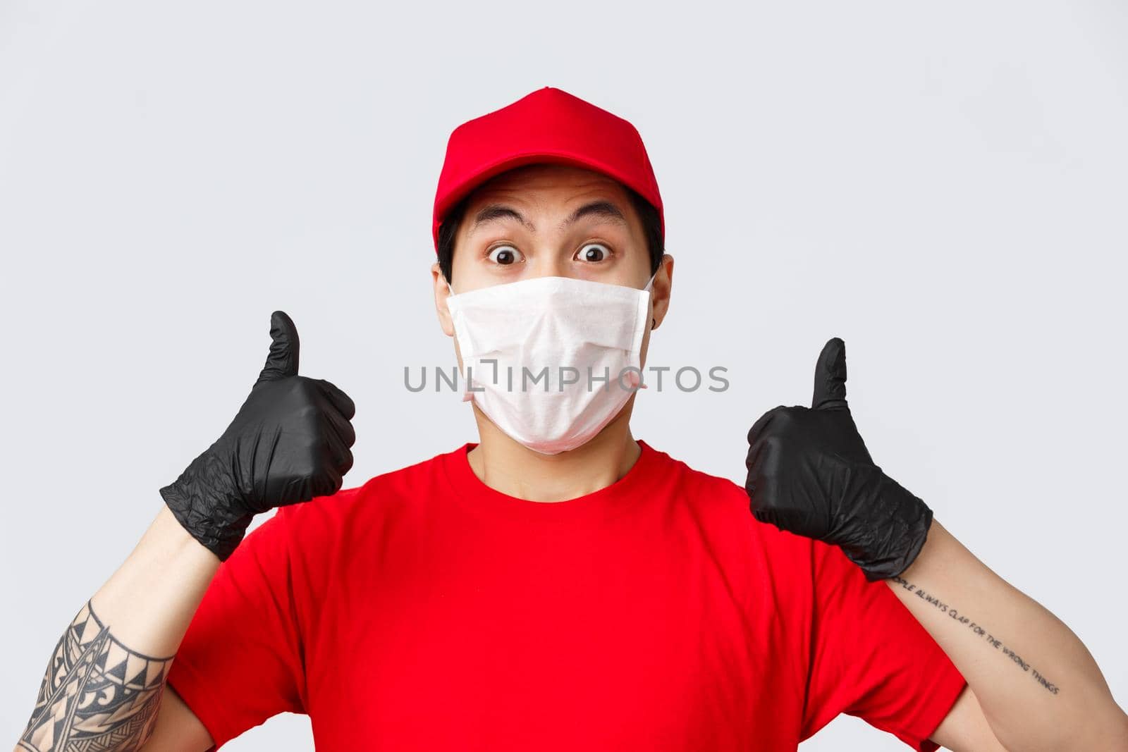 Covid-19, self-quarantine online shopping and delivery concept. Enthusiastic asian courier in red cap and t-shirt uniform, wear medical mask and gloves, thumb-up, recommend safe deliver.