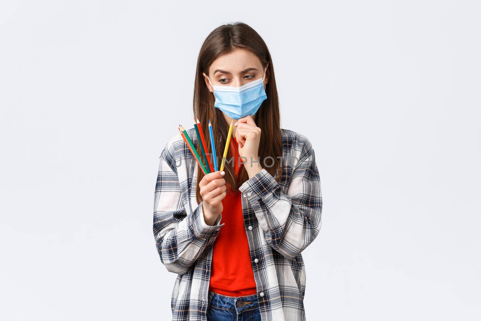 Social distancing, leisure, hobbies on covid-19 outbreak, coronavirus concept. Thoughtful cute girl in medical mask learn how draw on self-quarantine, wear medical mask, thinking as look at pencils.