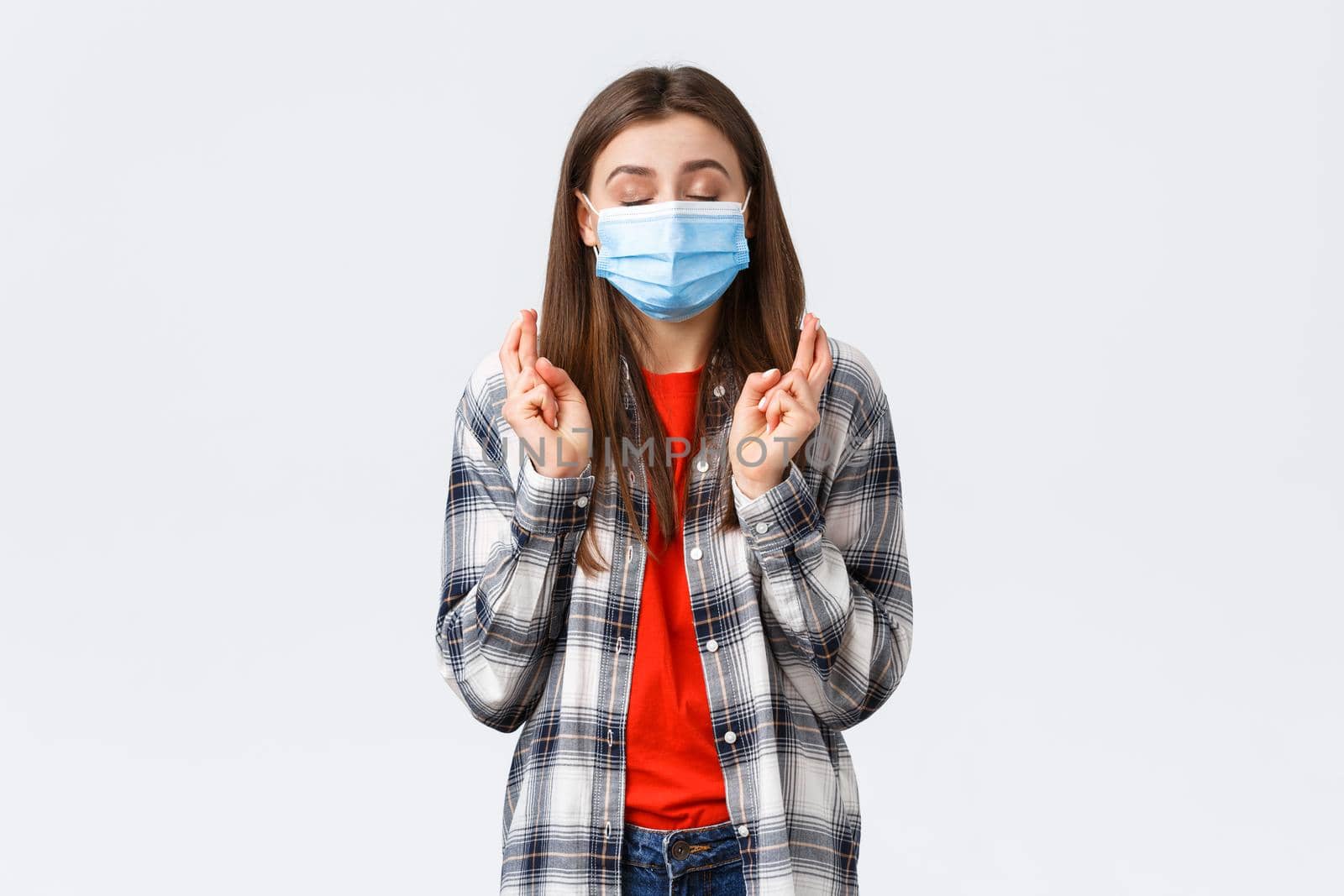 Coronavirus outbreak, leisure on quarantine, social distancing and emotions concept. Hopeful cute young woman in medical mask praying, close eyes and cross fingers good luck, making wish by Benzoix