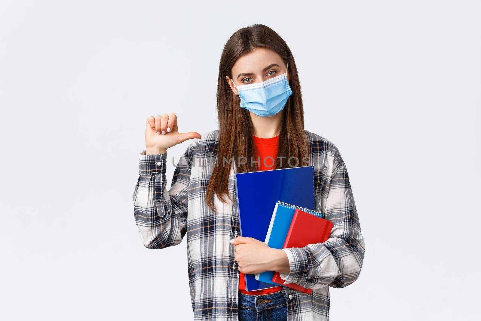 Coronavirus pandemic, covid-19 education, and back to school concept. Confident sassy female student pointing herself, wear medical mask, studying at university, holding notebooks.