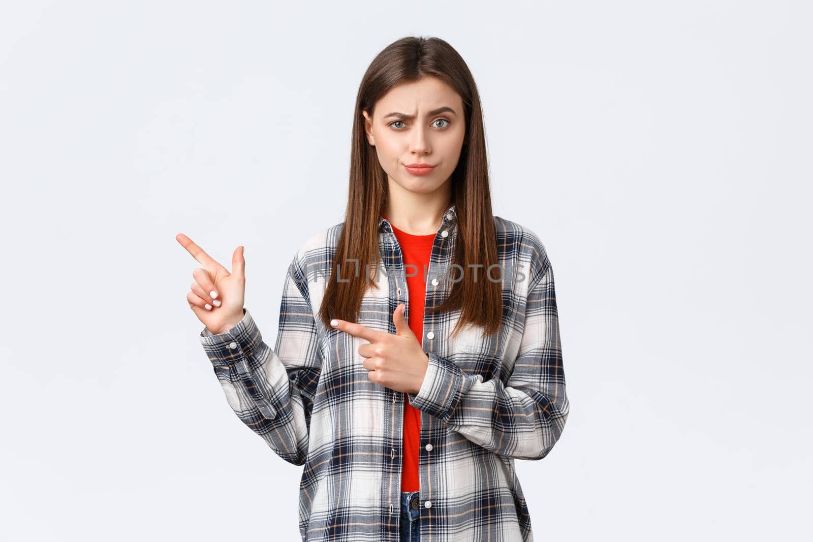 Lifestyle, different emotions, leisure activities concept. Skeptical and unimpressed girl having suspicious thoughts, express disbelief and skepticism, pointing fingers left and smirk displeased.